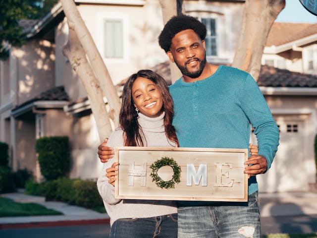 black woman and man holding home sign outside property