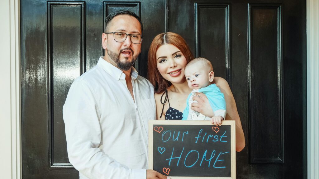 parents and baby holding first home sign